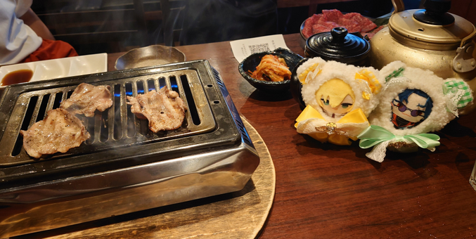 焼けてる肉（牛タン）、ついでにその横に卯月コウと魁星のぱぺ（にじさんじのグッズ）