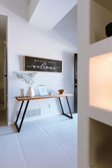 A photo of a modern-looking house, with a end table with a vase and other knick-knacks on it, with a hanging sign above it saying "Hello and Welcome". Photo by Rebeca Alvidrez on Unsplash