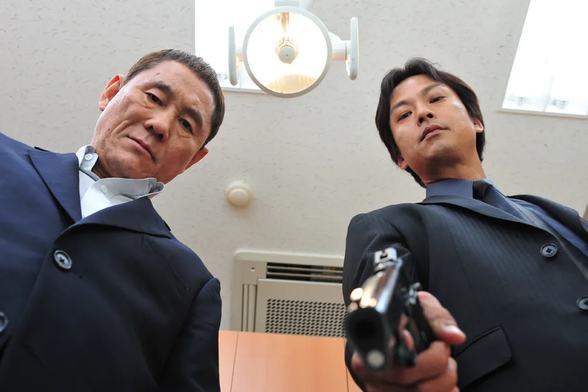 Scene from Outrage: Camera looking up at two men in suits, one holding a gun