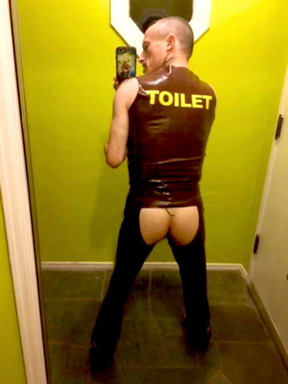 In brown rubber in my front entryway of my house. Chaps revealing ass. The word “TOILET” in letters across my back. Looking over left shoulder attempting a selfie in a mirrored door.