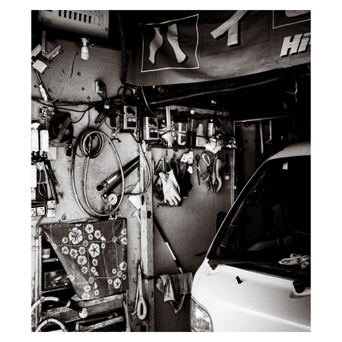 On one side, shelves and hooks hold an eclectic mix of wrenches, pliers, gloves, and cables—all organized with a method only the owner understands. A patterned cloth with a retro floral design hangs like a decorative afterthought.