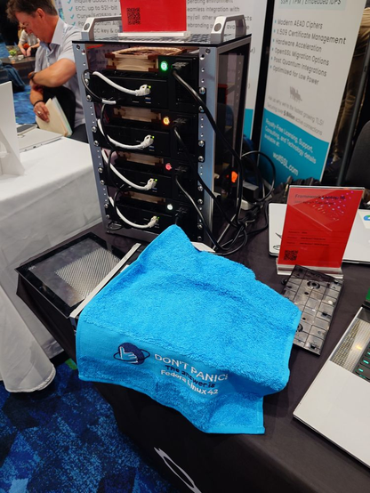 A Fedora branded towel for Fedora Linux 42 next to a rack of the new Framework Desktops.