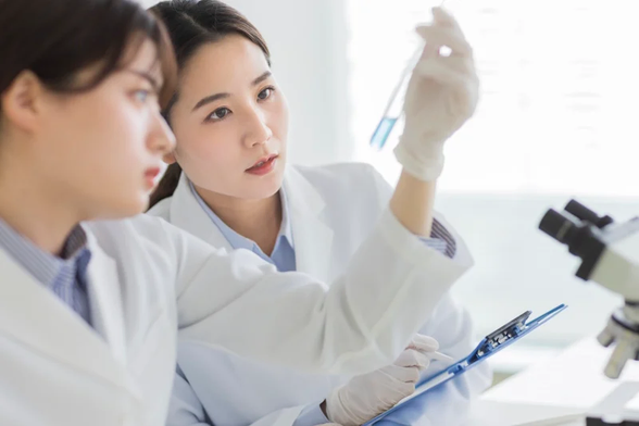 Two women in lab coats looking at a test tube vial
