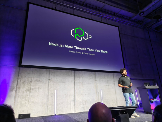 Picture of Matteo on Stage, in front of a slide with the text 
"Node.js : More Threads Than You Think"