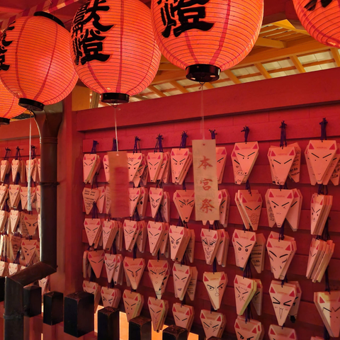 Kitsune (fox) votive tablets under red lantern light.