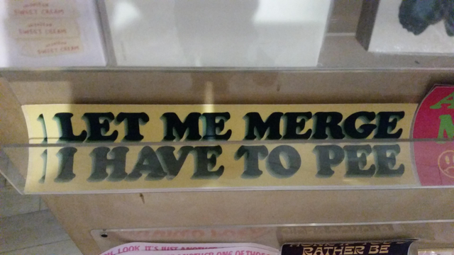 A bumper sticker in a bold serif font says "LET ME MERGE I HAVE TO PEE"