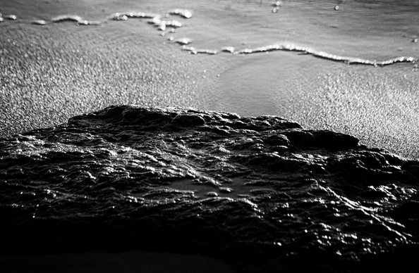 A simple black& white image of a rock shelf and water receding across the sand