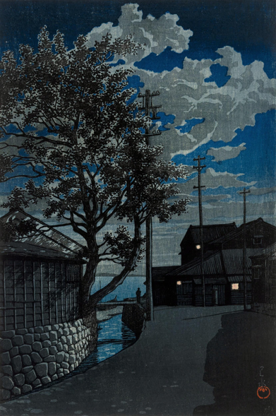 Evening in Kamezaki, in modern day Handa City, Aichi Prefecture. On our left, a narrow curving canal leads to what is probably Mikawa Bay; a tall wiry tree grows out of the space between a nearby building and the solid-looking stone embankment. On our right, a deserted street reaches a dead end in the direction of the water, and makes a 90 degree turn out of frame. An electric outdoor light shines outside the house standing on the end of the street, with another on a utility pole nearby; warm light glows in one of the windows of the house. The shadowy shape of a person stands between the house and the canal, looking out over the bay beyond, where a small wooden boat has been pulled up on the shore. Further on, the calm water stretches out toward the horizon, and a distant line of low hills marks the other side of the bay. Above, puffy clouds populate a starless evening sky. The whole scene is illuminated by the unseen moon.