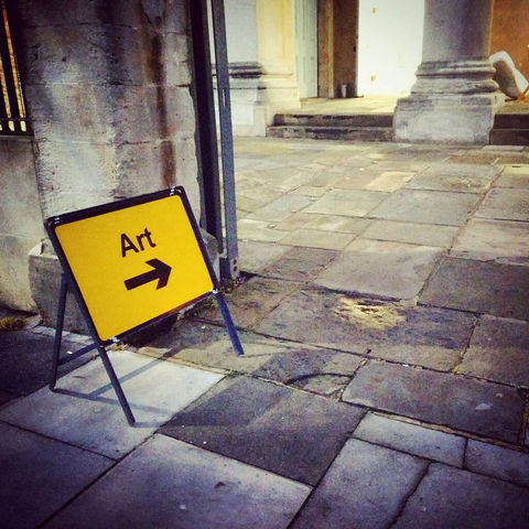 Un panneau de signalisation où est inscrit "art", avec une flèche directionnelle, posé sur le sol, à l'entrée d'une cour