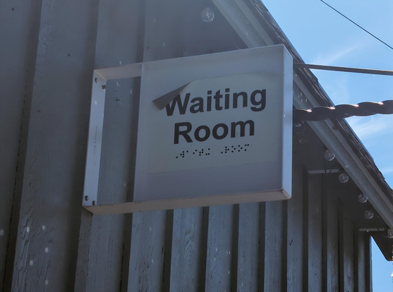 A sign on the side of a building; it reads "Waiting Room". There's braille below the writing. It's still about 10 feet off the ground.