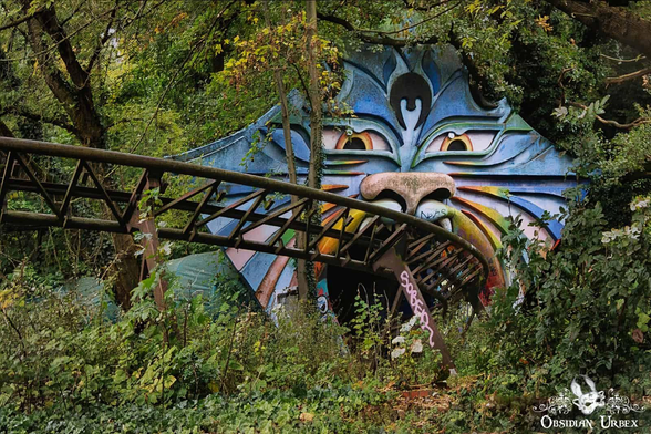 photo of an old rollercoaster, going into a tunnel. The tunnel is the mouth of a giant blue cat, with rainbow cheeks and eyes