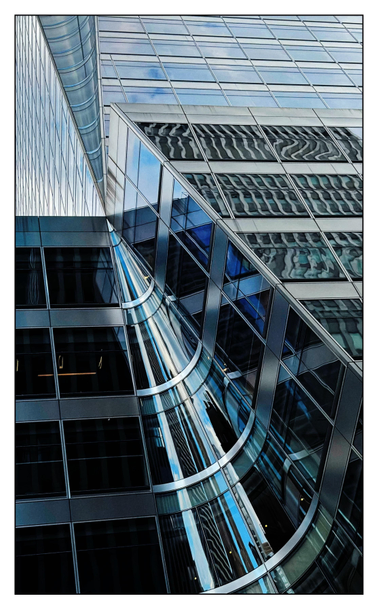 Closeup of the facade of the Bank of China office tower at 7 Bryant Park in Manhattan, a glass-and-steel skyscraper of many reflective windows, viewed from an askew angle at street level. The upper portion of the building is set back from the lower one. Strikingly, two conical incisions are carved into a corner of the tower: the lower cone pointing up, the upper one pointing down, narrowing to where their apexes meet at the setback level to create an hourglass effect. From the angle of the photo it also appears as a kind of starburst, with the building’s lines all converging on a vanishing point. The windows of the lower part of the tower reflect distorted images of other windows and buildings, while the upper part reflects white clouds in a blue sky.

h/t Architect Magazine for help with the description:
https://www.architectmagazine.com/project-gallery/bank-of-china-at-7-bryant-park/