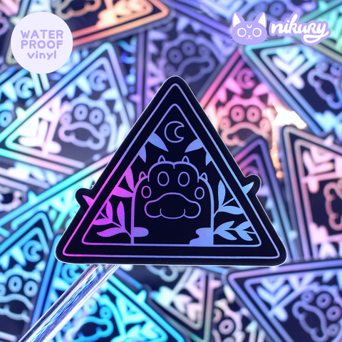 A picture of an illustrated vinyl sticker with a cat paw, moon and leaves inside a triangle. Colors are black with holographic details.