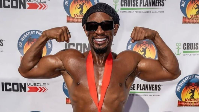 In this photo, a muscular man is smiling broadly while striking a double biceps pose, showing off his arms and physique. He’s wearing dark sunglasses, a black head covering, and a medal with a red ribbon hanging around his neck, signaling his placement in a bodybuilding competition. Behind him is a step-and-repeat banner with logos including ICON Muscle, Cruise Planners, and the Venice Muscle Beach branding, which is well-known for hosting bodybuilding contests.

This is rapper Lil Jon, who placed third in the Muscle Beach Venice competition. The image captures both his personality and his achievement, blending his trademark energetic vibe with the competitive world of bodybuilding.