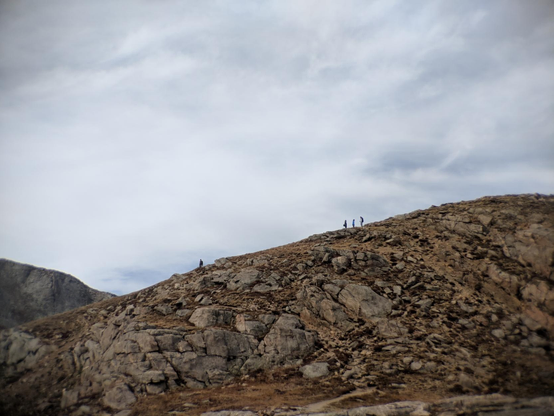 Four people silhouetted against a bright sky as they walk the path to the summit