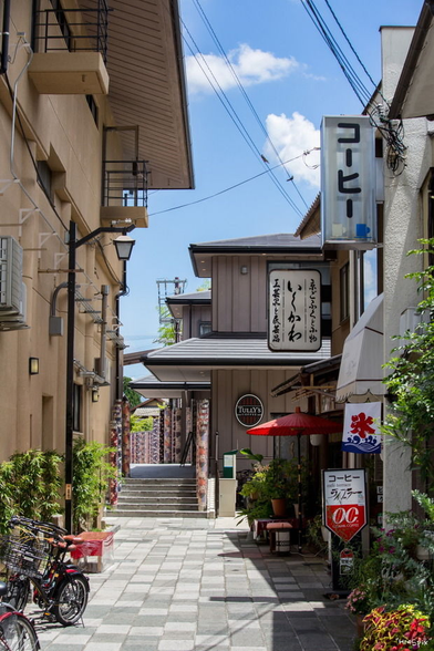 Japanese street with a bright sun and a lot of signage. Stairs at the back leads to a train station.