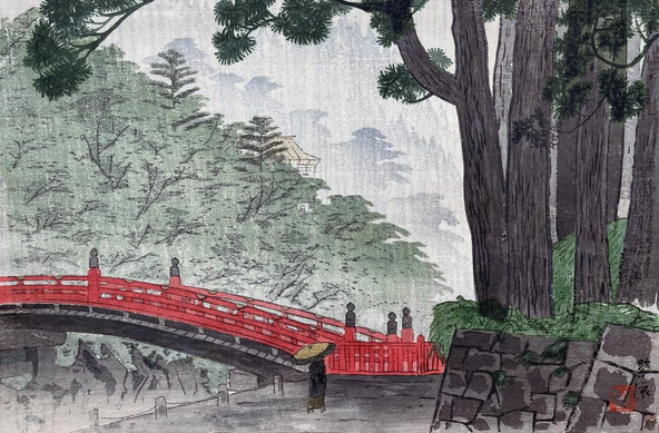 A rainy day in Nikko, looking toward the famous Shinkyo bridge. On our right, our view is framed by tall pine trees growing on top of a solid stone embankment; up ahead, a lone pedestrian carrying an umbrella approaches the red-lacqured bridge crossing the gorge. Beyond, healthy looking trees cover the the steep hillsides leading down toward the Daiya River below. Rain continues to fall across the scene.