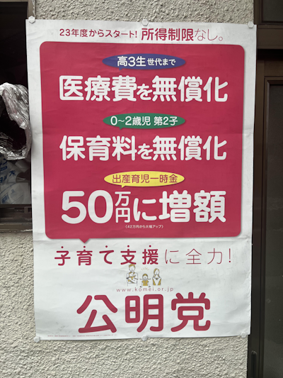 The Kōmeitō poster above touts new policies that started in 2023, including free medical care for kids up to the third year of high school, free daycare for a family’s first two children until age 2, and a one-time 500,000 yen ($3,380) payment at birth.
