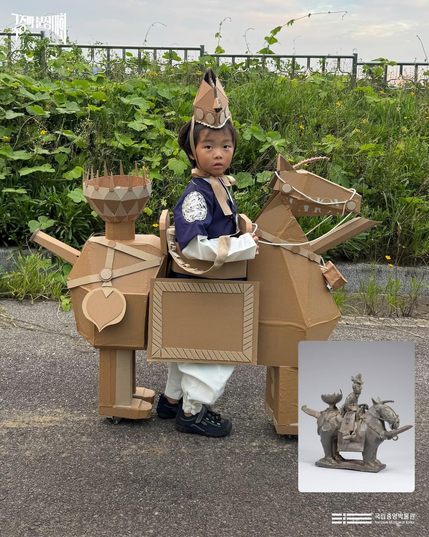 An ornate horse made out of cardboard with lots of small decorative elements and a child is the rider, walking and holding it up. Inset image shows the inspiration, which is a small earthenware funerary statue of a very ornate horse and rider. 