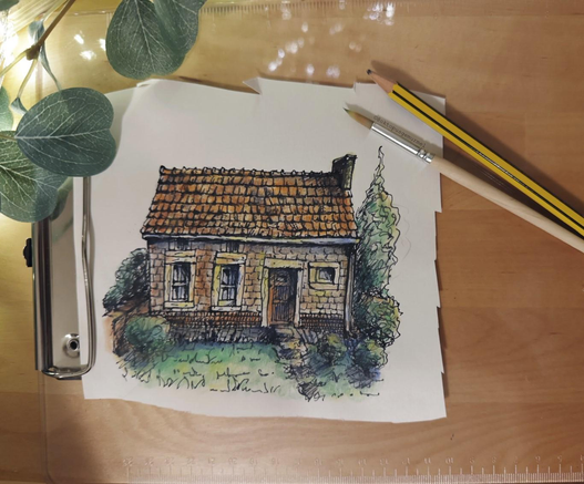 Ein Klemmbrett auf einem Tisch liegend, darauf ein Bild, ein Pinsel und ein Bleistift. Auf dem Bild ist ein Steinhäuschen mit Garten zu sehen.