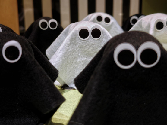 A photo showing a group of small black and white fabric figures with large googly eyes arranged closely together.

