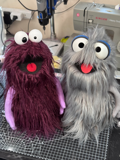 Two small muppet like hand puppets, one with purple fur and one with grey fur
