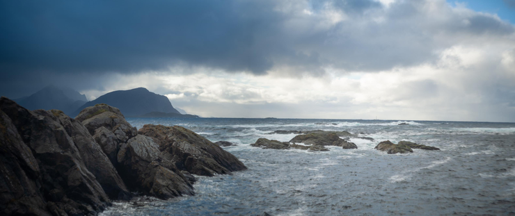 Jagged rocks sticking out of a stormy sea, dark clouds and specks of blue sky, dramatic lighting