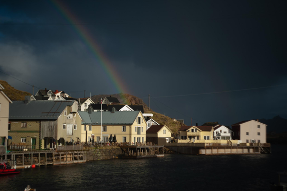 a small old fishing village by the sea, dark clouds, dark sea, dramatically lit from the side, rainbow in the background