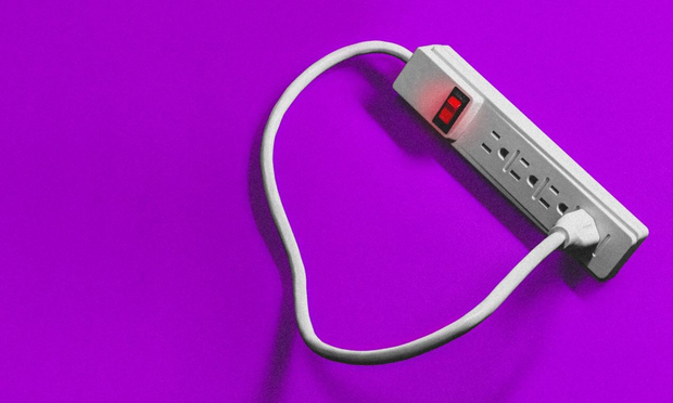 This is a studio-style photograph of a white power strip lying on a vibrant, solid purple background. The power strip has a red, illuminated "on" switch at the top. The power strip's own white cord is plugged into one of its own sockets, creating a closed loop. The object is lit from the side, casting a soft shadow onto the purple surface.