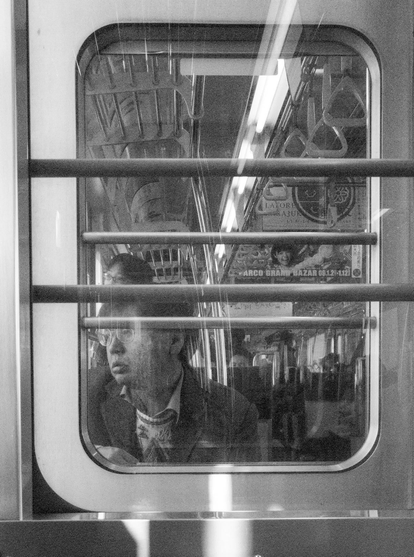 black and white photograph of a despondent looking man staring out of a train window, taken from the next carriage