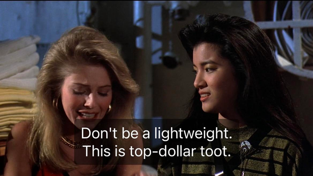 Two women are engaged in a conversation. One woman, with blonde hair, appears distressed while the other woman, with dark hair, looks at her with a serious expression. The background includes folded towels and various objects, suggesting an indoor setting. Subtitles say don’t be a lightweight, this is top dollar toot 