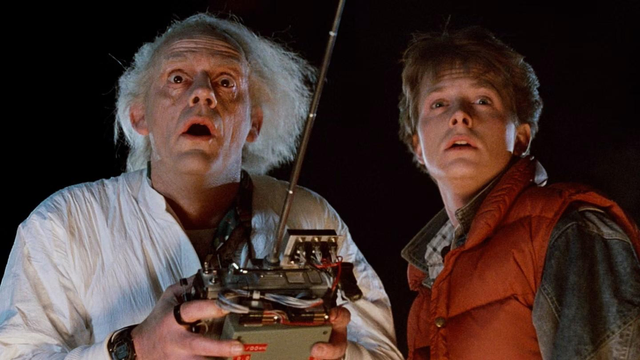 Christopher Lloyd as Doc Brown and Michael J. Fox as Marty McFly from Back to The Future. Doc is holding a large controller in his hands as they are both staring in front of them in awe.