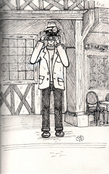 Dessin à l'encre et en noir et blanc d'un homme muni d'un ancien appareil photo avec un gros flash devant une maison ancienne en bois et à colombage. A droite, une terrasse de café.

Ink and black and white drawing of a man with an old camera with a large flash in front of an old wooden and half-timbered house. To the right, a café terrace.
