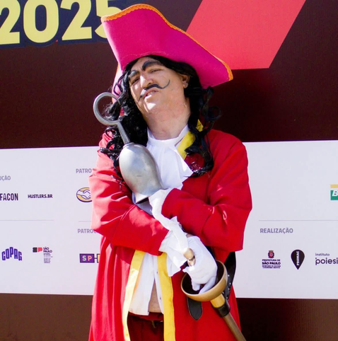 Um homem fantasiado de Capitão Gancho está em pé em frente a uma parede com logotipos e texto. Ele está vestindo uma camisa branca com um colete vermelho, calças vermelhas e um chapéu preto. O homem tem uma barba escura e um bigode e está segurando um sabre na mão direita. A parede atrás dele tem vários logotipos e o texto "2023". Na parte inferior da parede, há os logotipos "COP28" e "PREFEITURA DE SÃO PAULO" e "Instituto Poiesi". O logotipo "Hustlers.BR" também está visível.

Fornecido por @altbot, gerado localmente e de forma privada usando Gemma3:27b