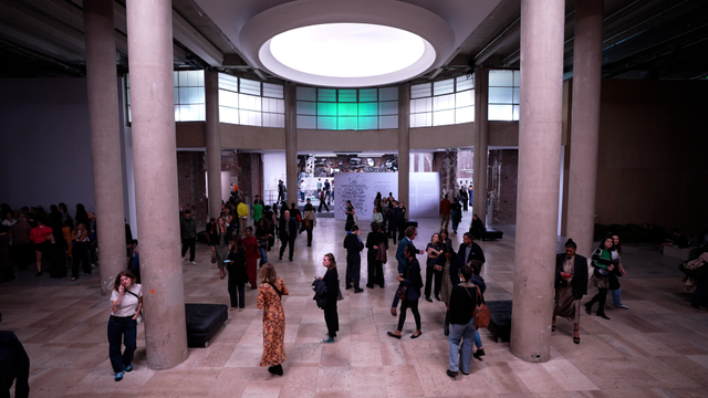 Vue intérieure du Palais de Tokyo à Paris, montrant un grand hall lumineux avec de hauts piliers en béton. De nombreux visiteurs déambulent, discutent et observent l’espace d’exposition au fond, sous un large puits de lumière circulaire.
