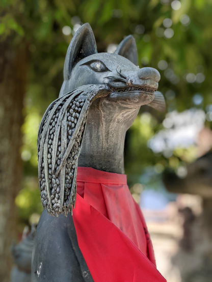 A statue of a kitsune holds an ear of rice in its mouth.