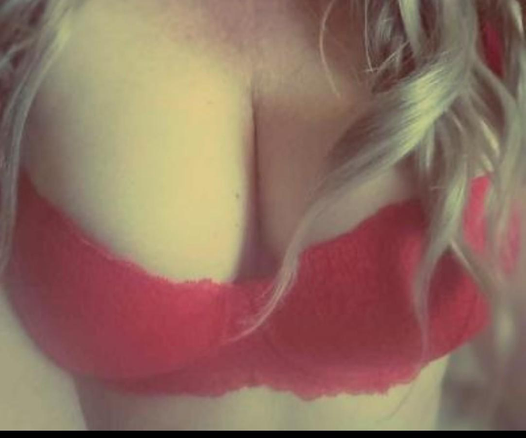 A closeup of my breasts in a red bra. I have long blonde wavy hair that falls gently over one breast. You can see my cleavage, and the fullness of my amazing titties.