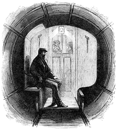 A workman sits in a rather small “omnibus” or railway carriage, seemingly outside the door on a bench, his booted feet resting on an extension of the carriage floor that reaches two railway wheels. This was a narrow-gauge train. He is not well lit, but through the glass window in the wooden door behind him we see people inside the carriage itself.