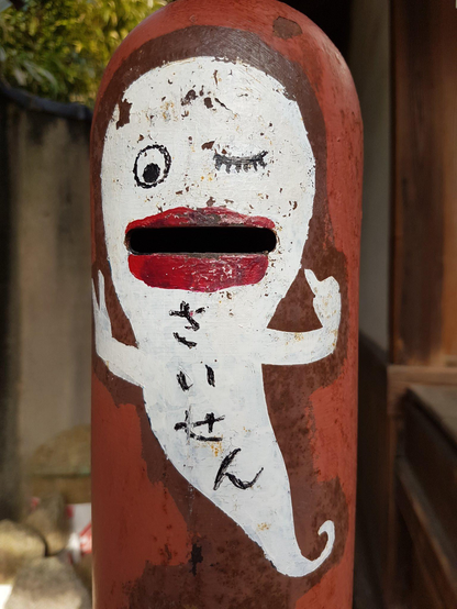 An offertory box painted with a ghost. Visitors place coins in the ghost's mouth before praying.