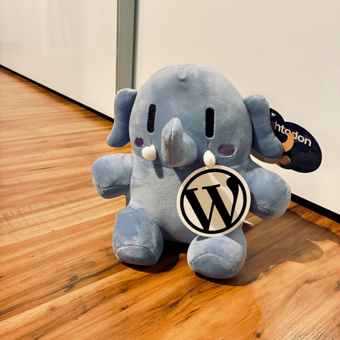 A Plush Mastodon holding a WordPress Sticker