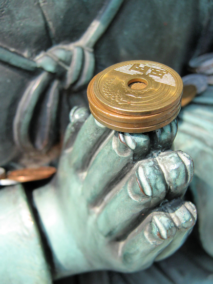 An offering of 5 yen coins left on the praying hands of a statue at Chion-in.