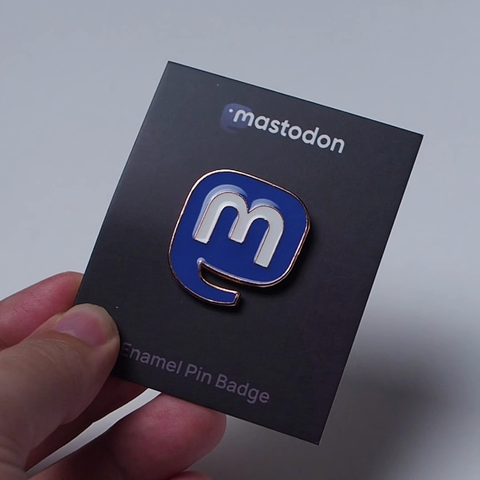 Me demonstrating the shiny finish of the Mastodon logo pin by moving it around in front of a plain white background.