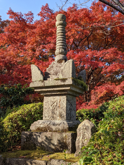 A stone memorial tower before a background of red leaves.
