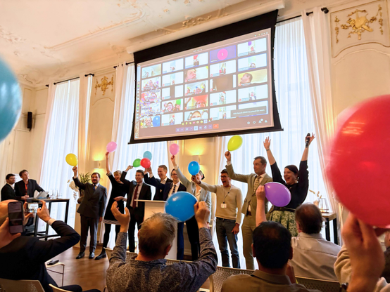 At the launch of the Digital Commons EDIC in the Hague, around a dozen people are standing in an ornate room cheering. Both they and many members of the audience are holding brightly colored balloons, while many others in a video call are projected on a screen above their heads.
