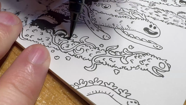 A closeup of a sketchbook. A hand is aplying black ink to the background of an illustration os weird and whimsical vegetal worm-like happy creatures. It is using a brush pen. Inking is slow, as it needs precission to fill the intrincate spaces.
