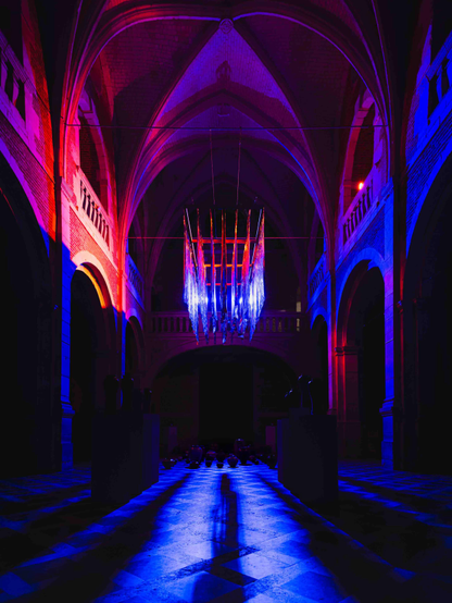 une exposition à l'intérieur d'une église, avec une sculpture lumineuse rouge et bleu, des céramiques au sol et la lumiere à travers la nef.
