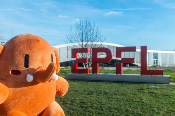 Plushtodon devant le logo de l'EPFL. En arrière-plan, le Rolex Learning Center