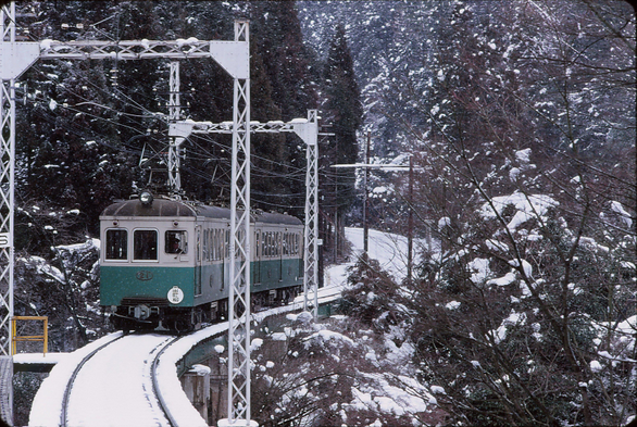 A train on the Eizan Line winds through a snowy landscape.