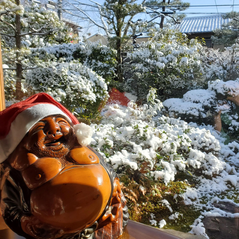 A cheerful statue of Hotei is Santa hat admires the teahouse's snowy garden.