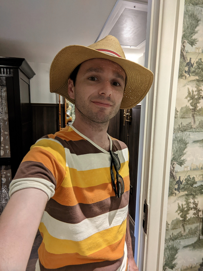 It is me.

I am wearing a summer hat and have a t-shirt adorned with white, yellow, orange and brown stripes. A pair of sunglasses are hanging from the collar.